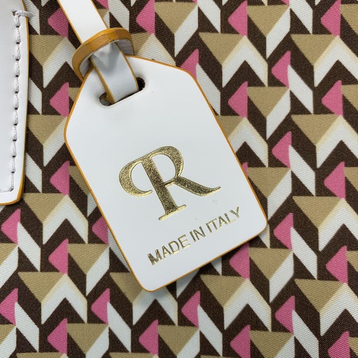 白色 Roberta Pieri 行李牌的特寫，上面有金色字母“R”和“MADE IN ITALY”字樣，貼在帶有棕色、米色和粉紅色幾何圖案的迷你行李袋上。