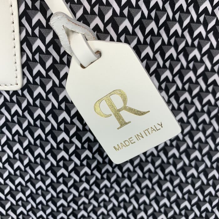 黑色和白色幾何織物的背景上懸掛著帶有金色字母“R”和“MADE IN ITALY”字樣的白色皮革 ROBERTA PIERI 標籤。